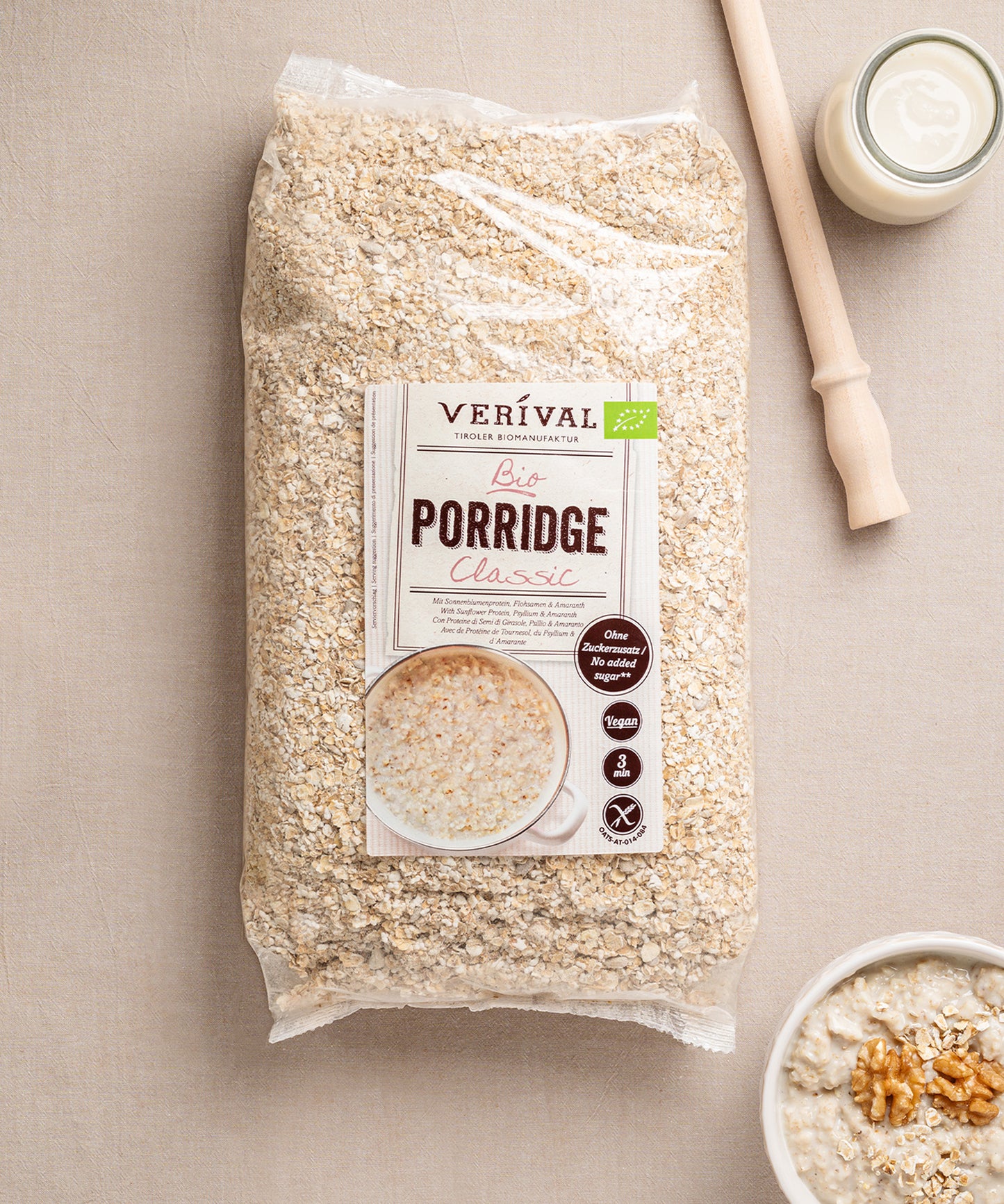 Eine Packung glutenfreies Classic Porridge von Verival Bio steht auf einem beigen Untergrund. Daneben steht eine Schüssel des herzhaften, ballaststoffreichen Porridges, garniert mit Walnüssen und einer Flasche Milch – für einen gesunden Start in den Tag.