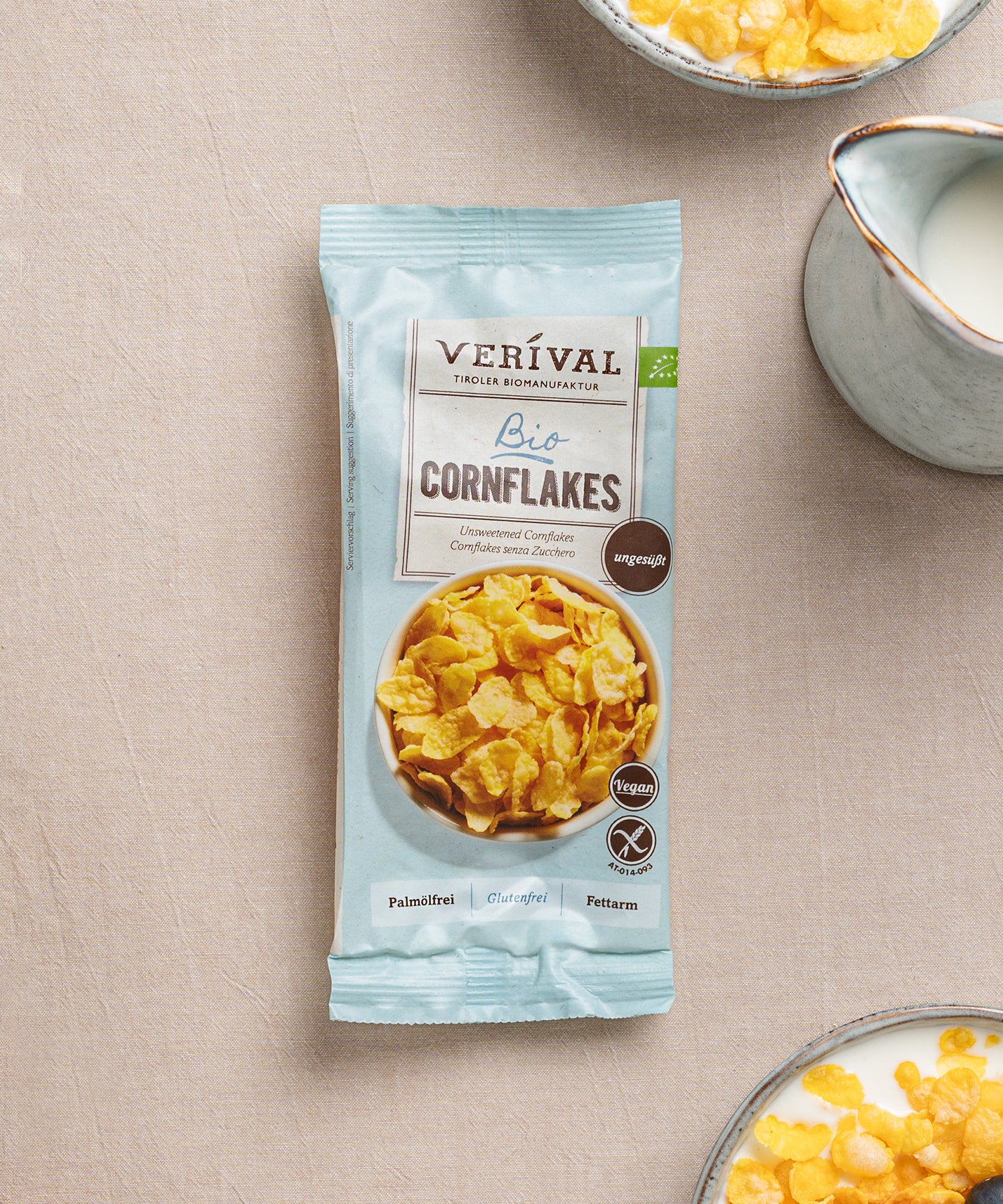 Auf einem Tisch steht eine Einzelportionspackung ungesüßte Cornflakes knusprige Frühstücksoption, daneben Schüsseln mit diesen knusprigen Leckereien, Milch und frischen Beeren.