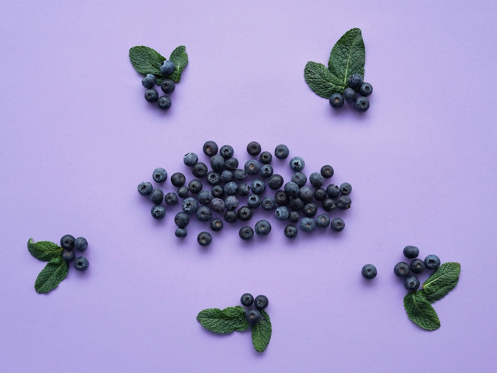 Des myrtilles et des feuilles de menthe sont disposées sur une surface violette.