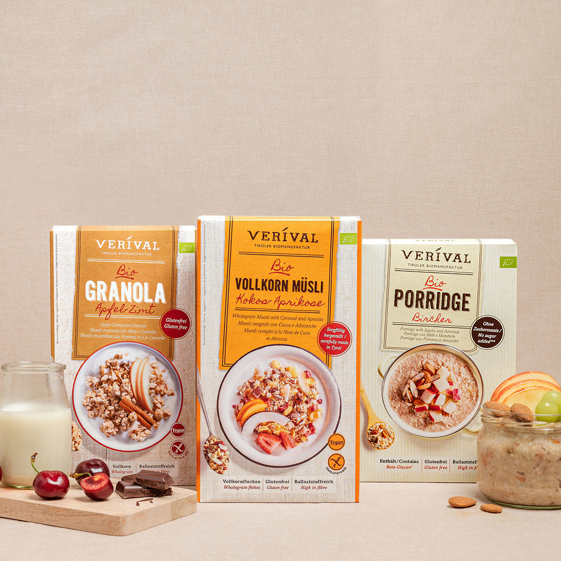 Trois boîtes de céréales étiquetées Crunchy, Wholegrain Muesli et Porridge sont présentées avec un verre, des cerises et des amandes sur un fond beige.