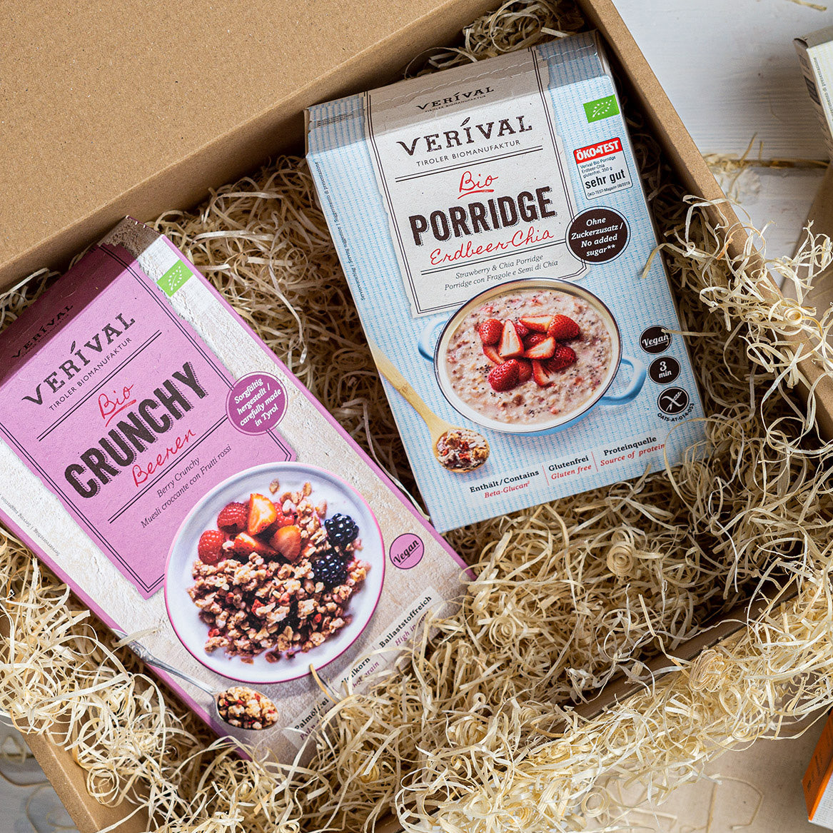 Verival Granola und Porridge-Packungen  liegen auf Holzwolle in einer Geschenkset-Verpackung. 